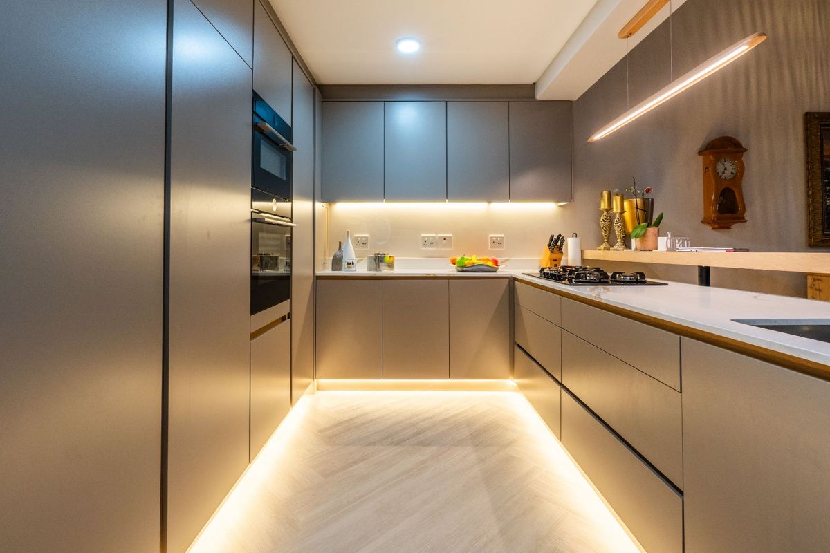 Modern galley-style kitchen featuring sleek handleless cabinetry, integrated oven, gas cooktop, and ambient under-cabinet and floor-level LED lighting.