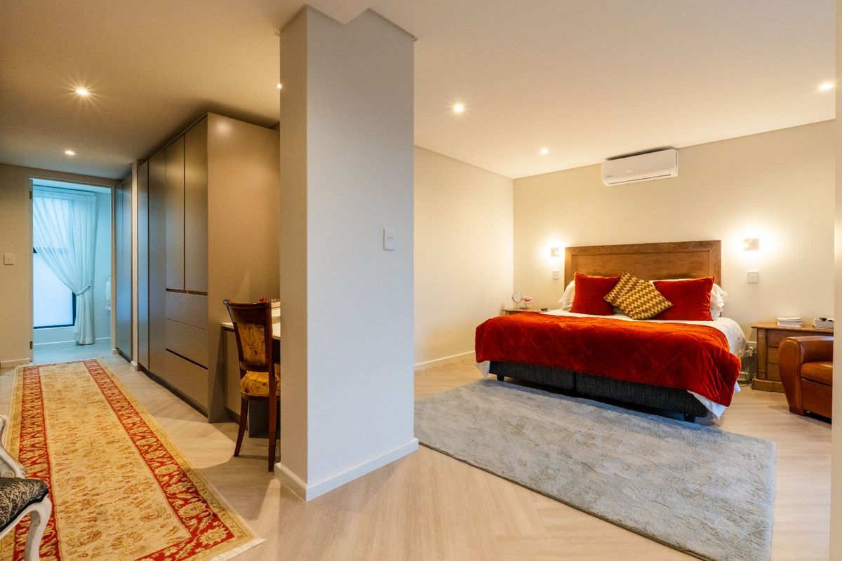 Spacious bedroom featuring built-in cabinetry, recessed downlighting, and a wall-mounted air conditioning unit, with an adjoining walk-through area.