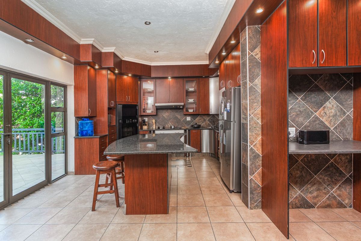 Spacious kitchen featuring dark wood cabinetry, granite countertops, a central island, tiled flooring, and direct access to an outdoor patio area.