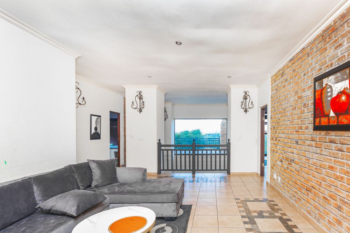 Spacious living area featuring a prominent exposed brick feature wall, tiled flooring, and an open transition to a balcony with scenic views.