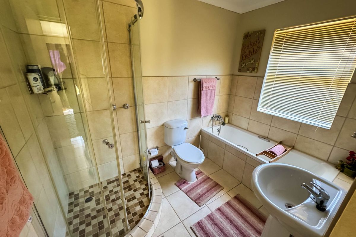 A functional bathroom featuring a corner shower enclosure, a standard bathtub, a pedestal basin, and tiled walls and flooring.