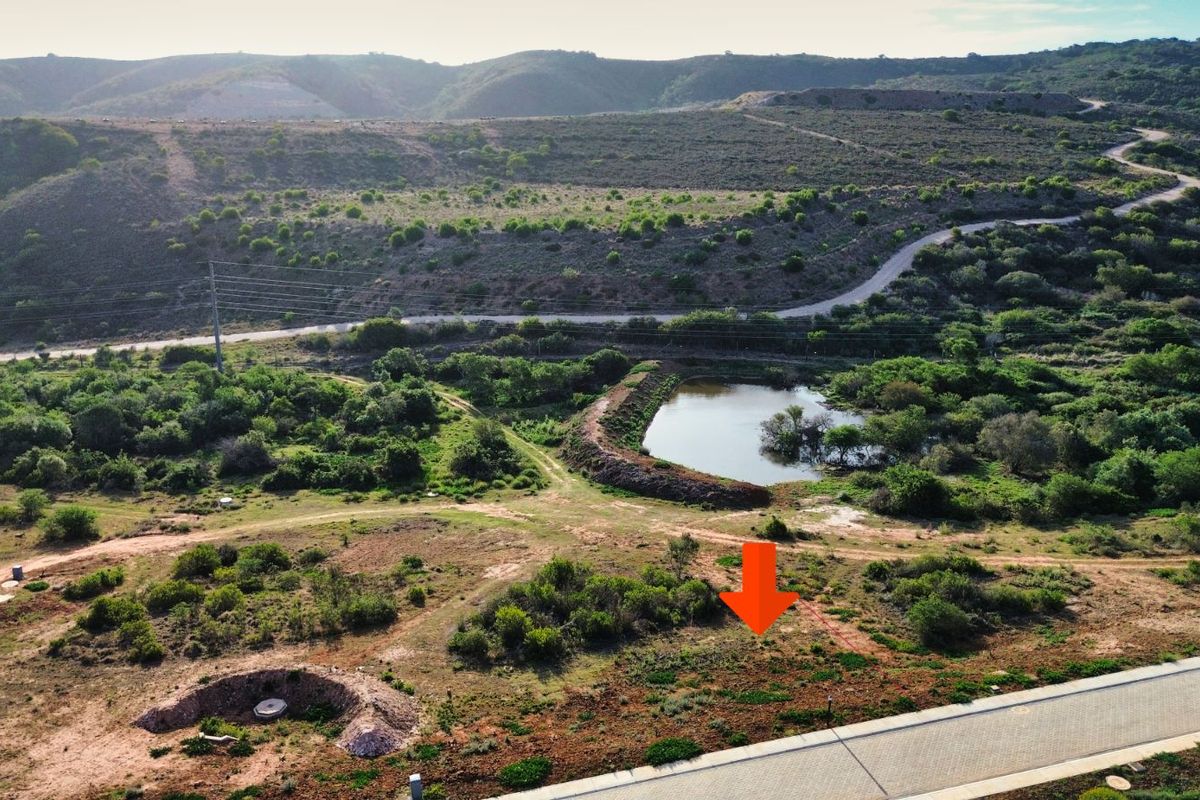 Aerial view of a vacant residential plot featuring natural landscape, nearby pond, and paved road access.