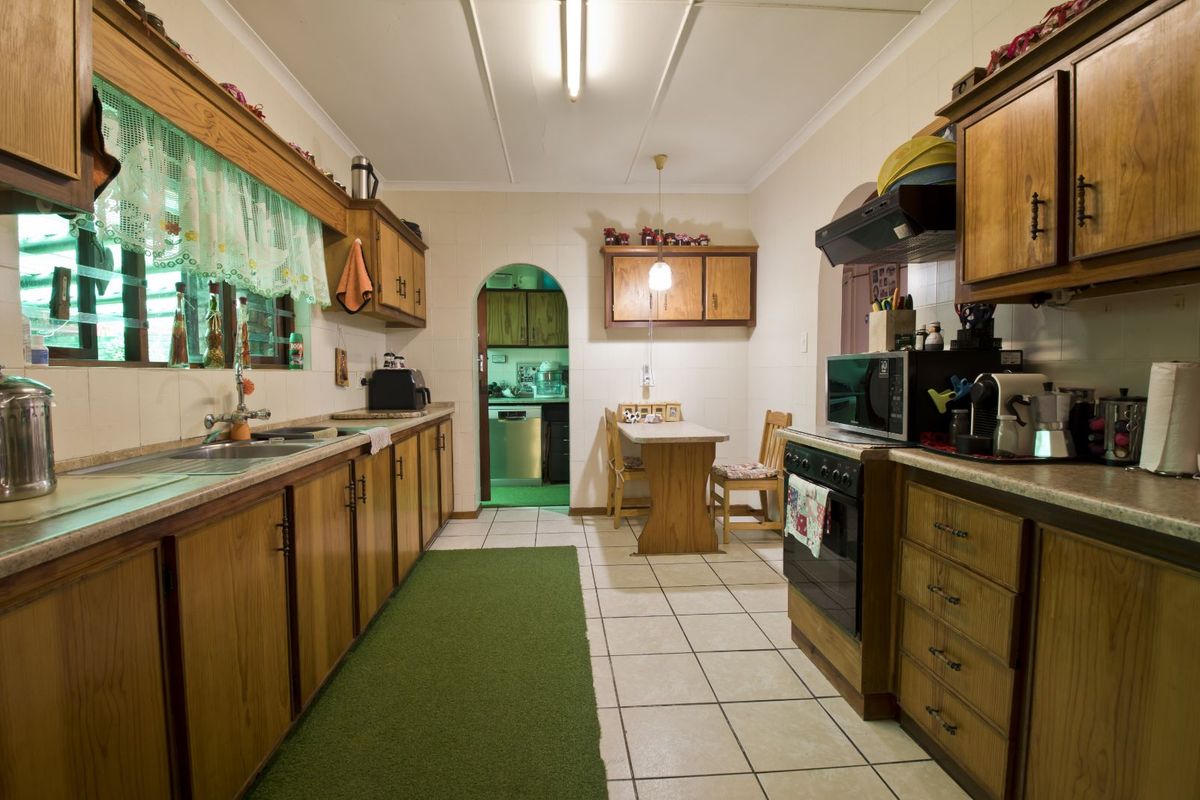 A functional kitchen featuring wooden cabinetry, tiled flooring, and a built-in oven with extractor fan, leading through an arched doorway to a secondary space.