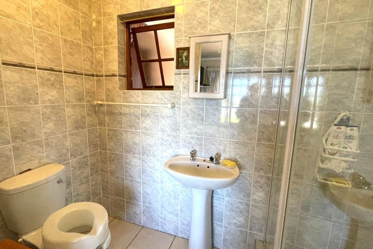 A functional bathroom featuring a pedestal basin, a toilet, and a glass-enclosed shower, finished with neutral wall tiles.