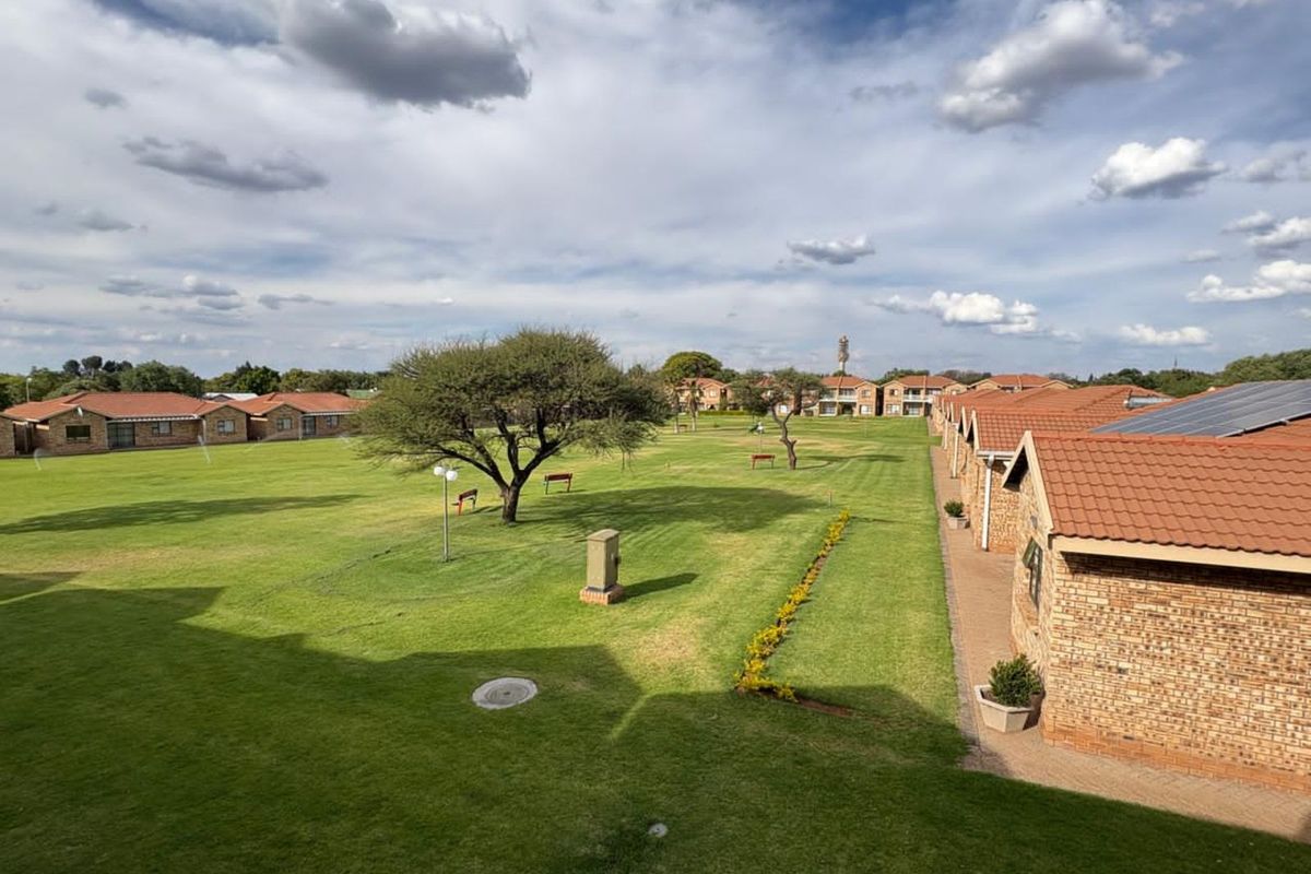 Elevated view overlooking a well-maintained communal garden area with expansive lawns and surrounding townhouse units featuring terracotta tiled roofs.