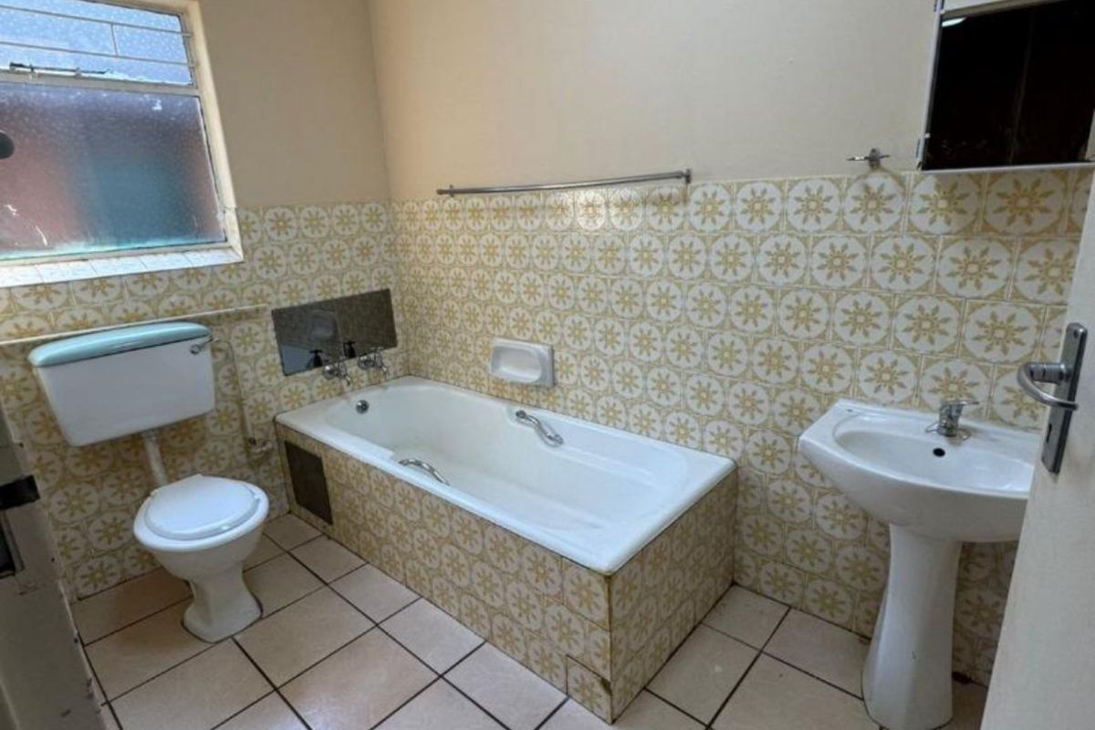 A dated bathroom featuring a standard bathtub, pedestal basin, and toilet with original patterned wall tiles and ceramic floor tiling.