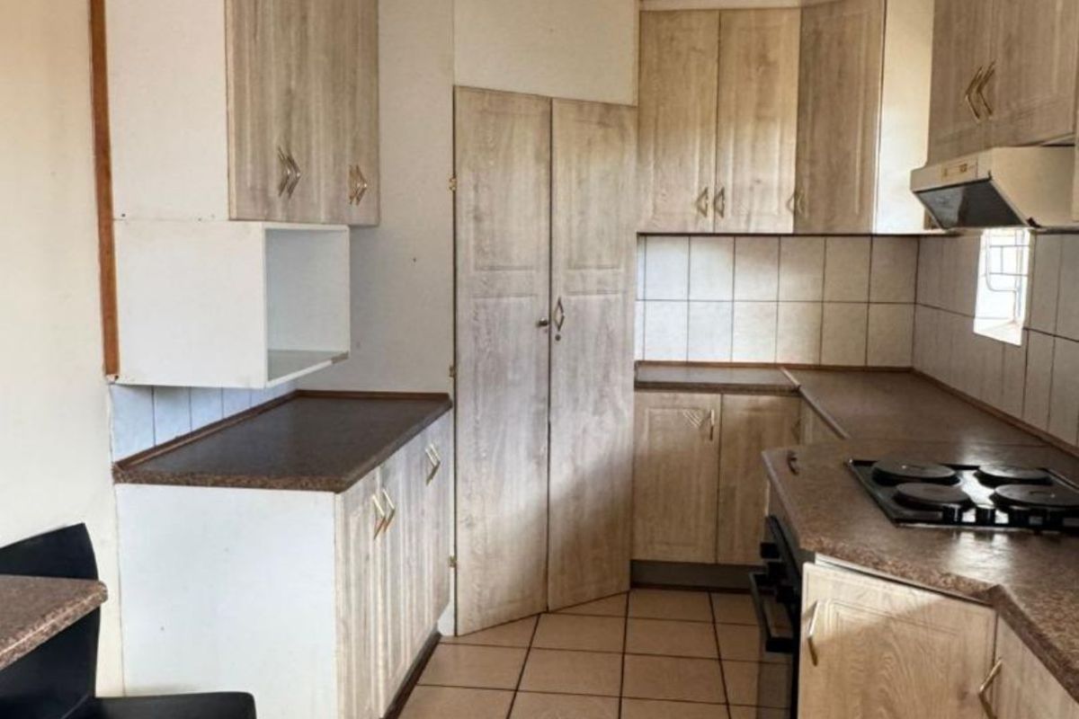 A dated kitchen featuring light wood-look cabinetry, tiled flooring, a built-in hob, and an extractor fan, offering potential for a modern renovation.
