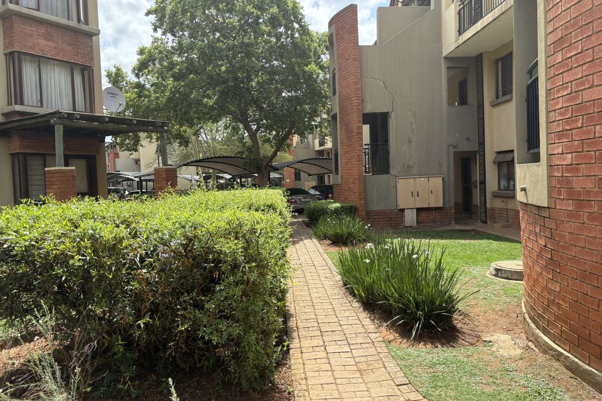 Exterior view of the apartment complex featuring a paved walkway, landscaped garden areas, and brick facade architecture.