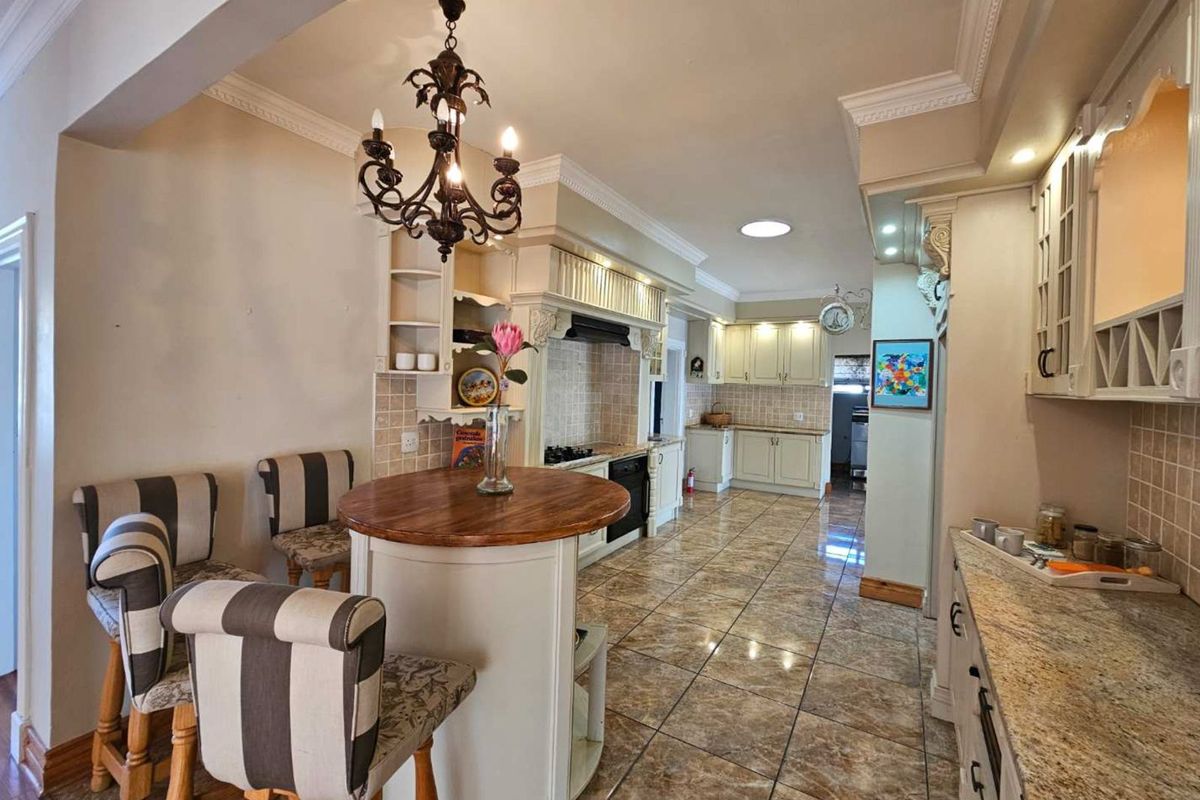 Spacious kitchen featuring classic cabinetry, granite countertops, tiled flooring, and a central breakfast island with overhead chandelier lighting.