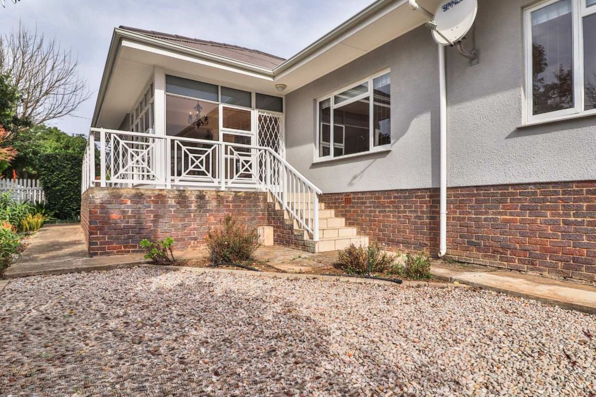 Rear exterior view of the house featuring a raised patio area with white railings, brick base, and gravel landscaping.
