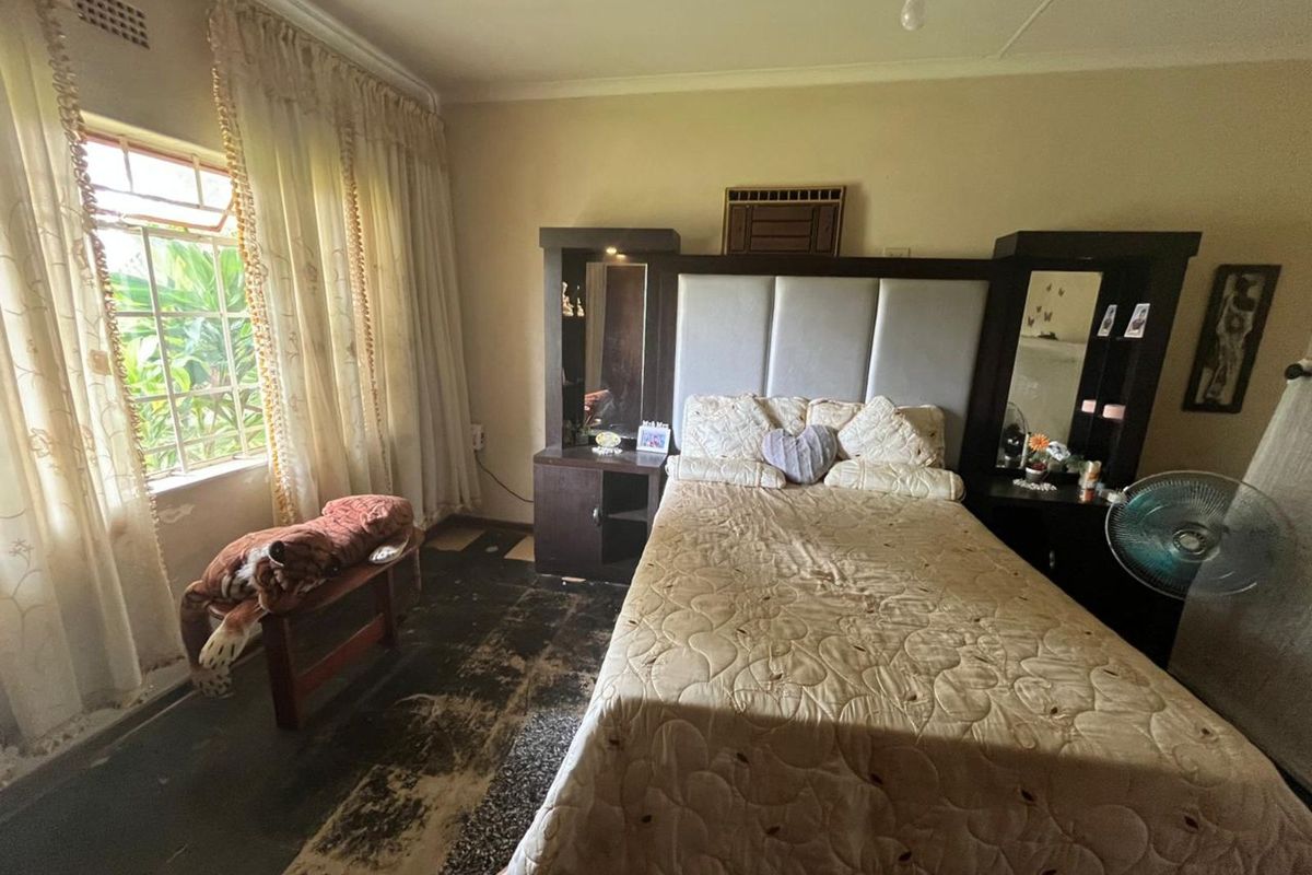 A bedroom featuring a built-in headboard unit with integrated mirrors and bedside storage, large window with natural light, and worn flooring.