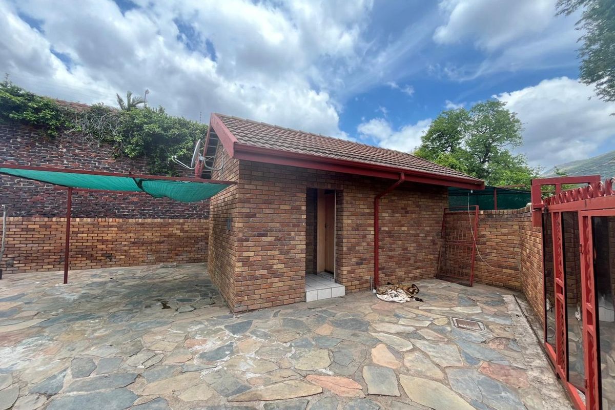 A detached brick outbuilding featuring a tiled roof, set within a paved courtyard area with perimeter brick walling and metal gate access.