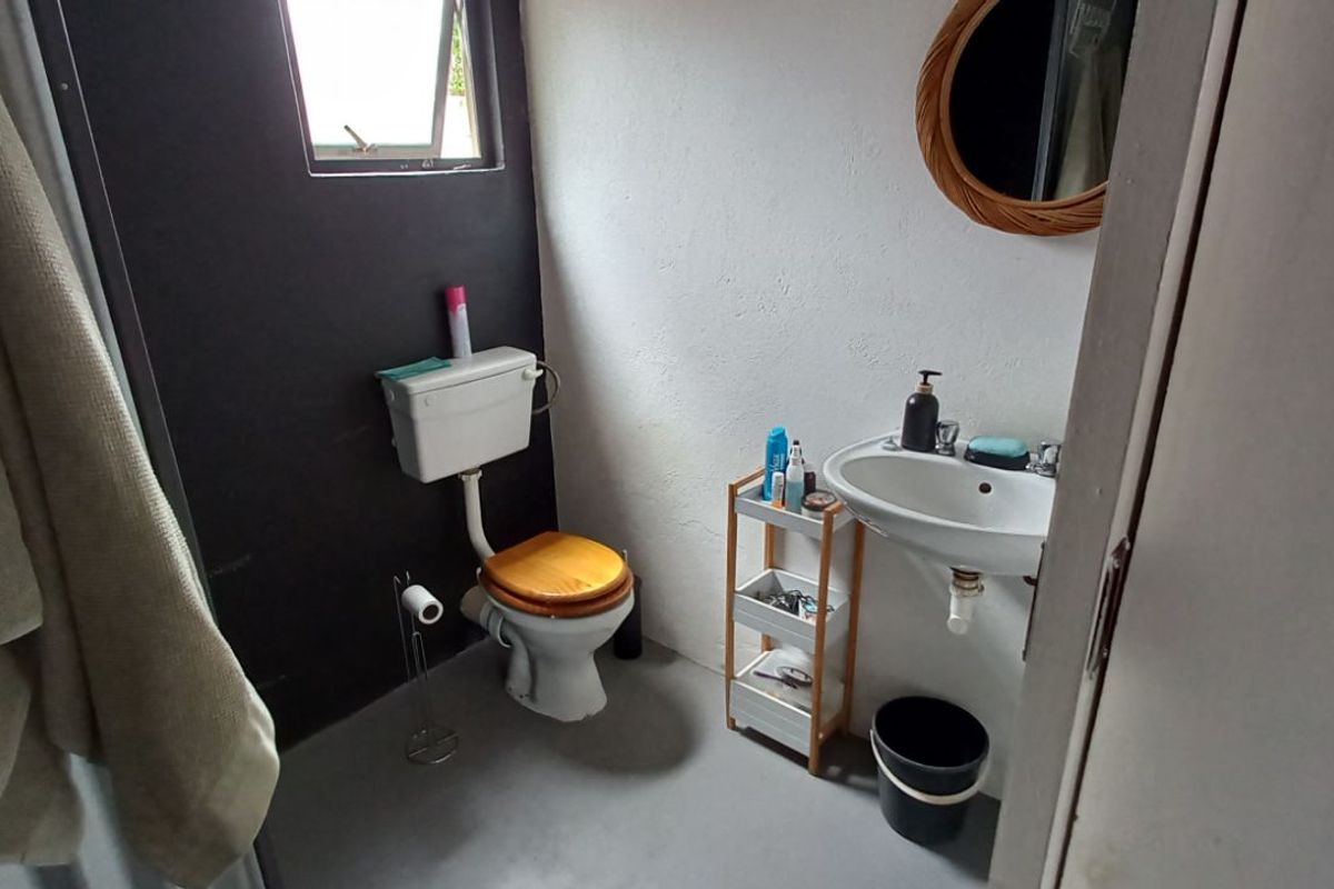 A compact bathroom featuring a wall-mounted basin, a traditional toilet with a high-level cistern, and a shower area.