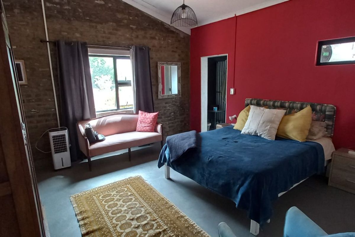 Spacious bedroom featuring exposed brick walls, polished concrete flooring, and a high vaulted ceiling with a modern pendant light fixture.