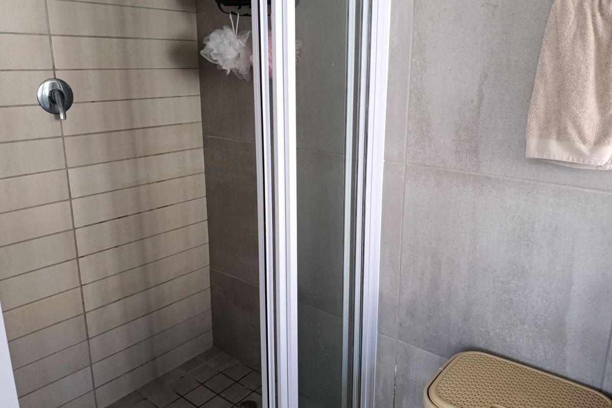 A functional bathroom shower enclosure featuring neutral wall tiling, a chrome mixer tap, and a folding glass shower door.