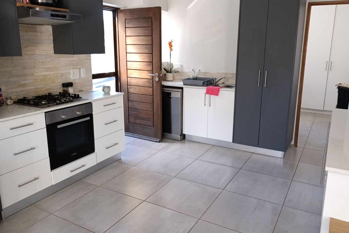 Modern kitchen featuring two-tone cabinetry, stone-look tiled flooring, built-in gas hob, electric oven, and extractor fan with direct access to the exterior.