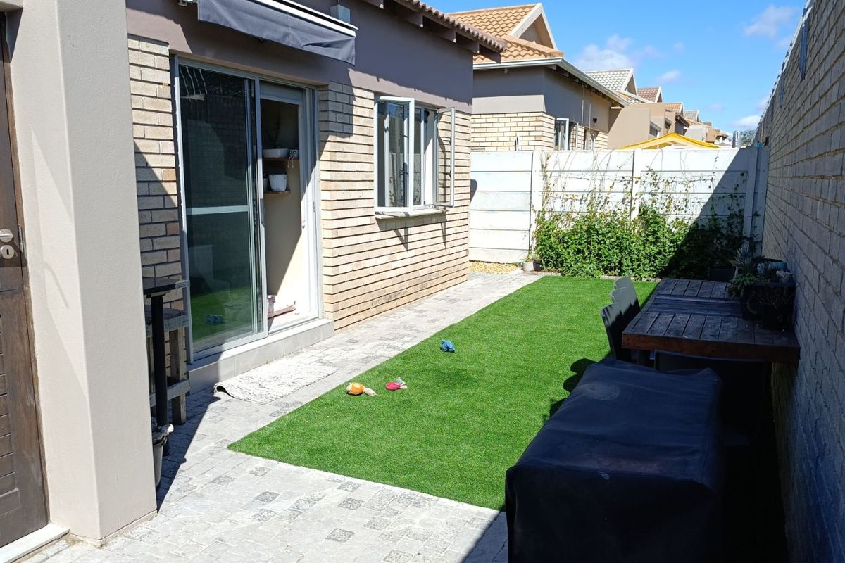 A private rear garden featuring a paved patio area, artificial lawn, and brick boundary walls, providing a low-maintenance outdoor space.