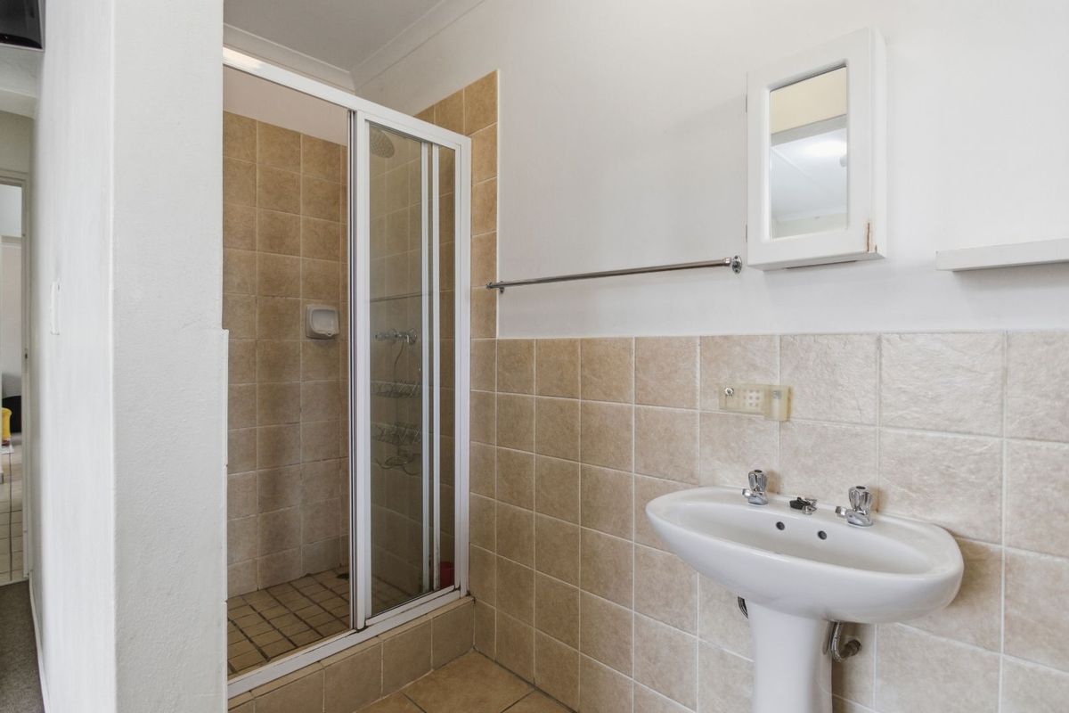 A functional bathroom featuring a pedestal sink, a glass-enclosed shower stall, and neutral wall tiling.