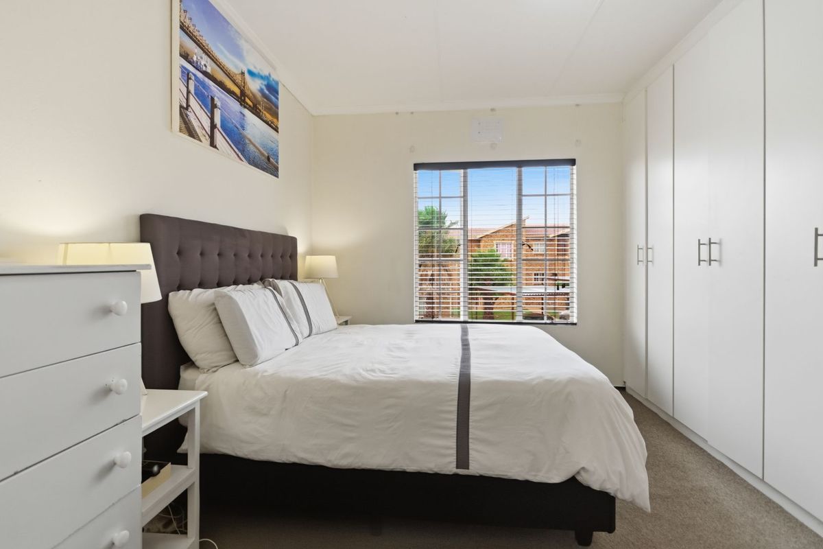 A well-maintained bedroom featuring neutral carpeting, built-in floor-to-ceiling wardrobes, and a window with fitted blinds providing natural light.
