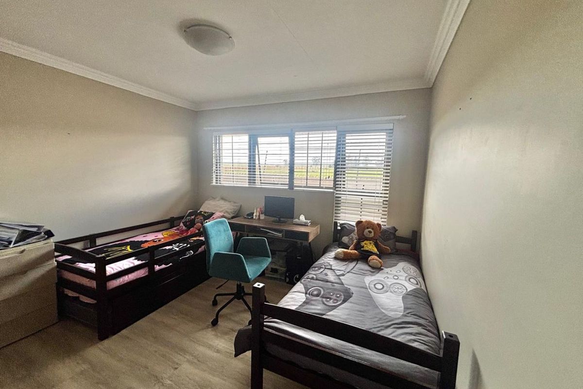 A functional bedroom featuring light-toned laminate flooring, crown molding, and horizontal window blinds, providing a comfortable space for rest or study.