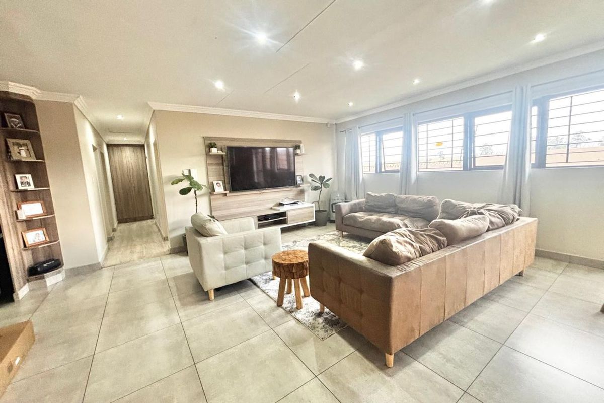 Spacious living room featuring large format floor tiles, recessed downlighting, and a built-in media unit with integrated shelving.