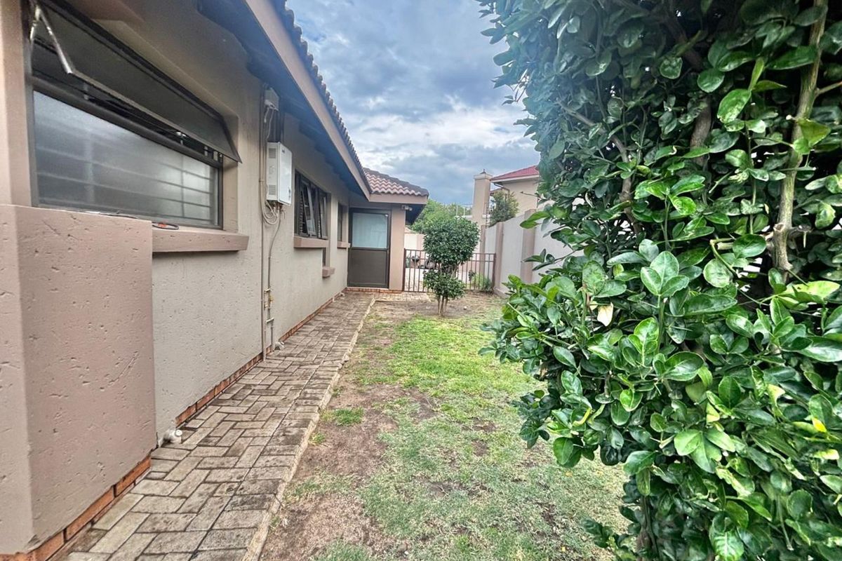A side view of the property featuring a paved walkway, exterior wall with window, and a small garden area.