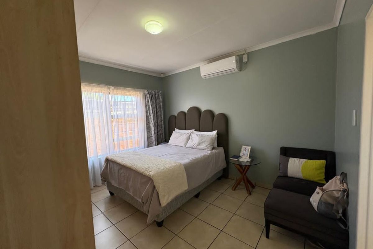 A well-lit bedroom featuring tiled flooring, a wall-mounted air conditioning unit, and neutral wall tones, providing a comfortable and functional living space.