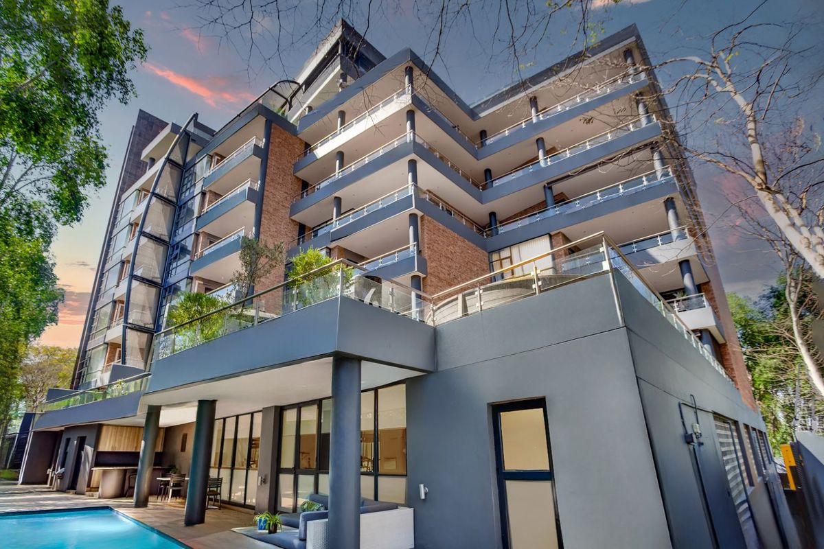 Modern multi-story apartment building featuring glass-railed balconies, brick and rendered facade, and a ground-level swimming pool area.