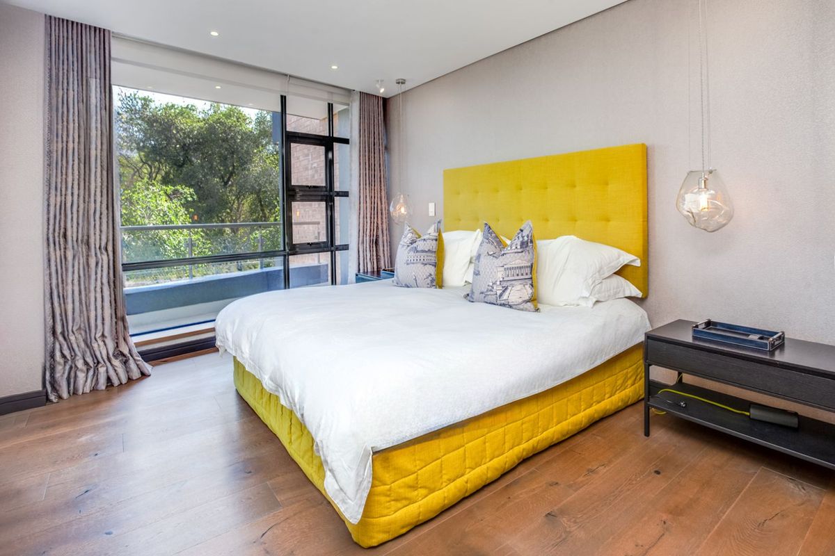 A modern, well-maintained bedroom featuring high-quality timber flooring, recessed ceiling lighting, and large floor-to-ceiling windows with integrated balcony access.