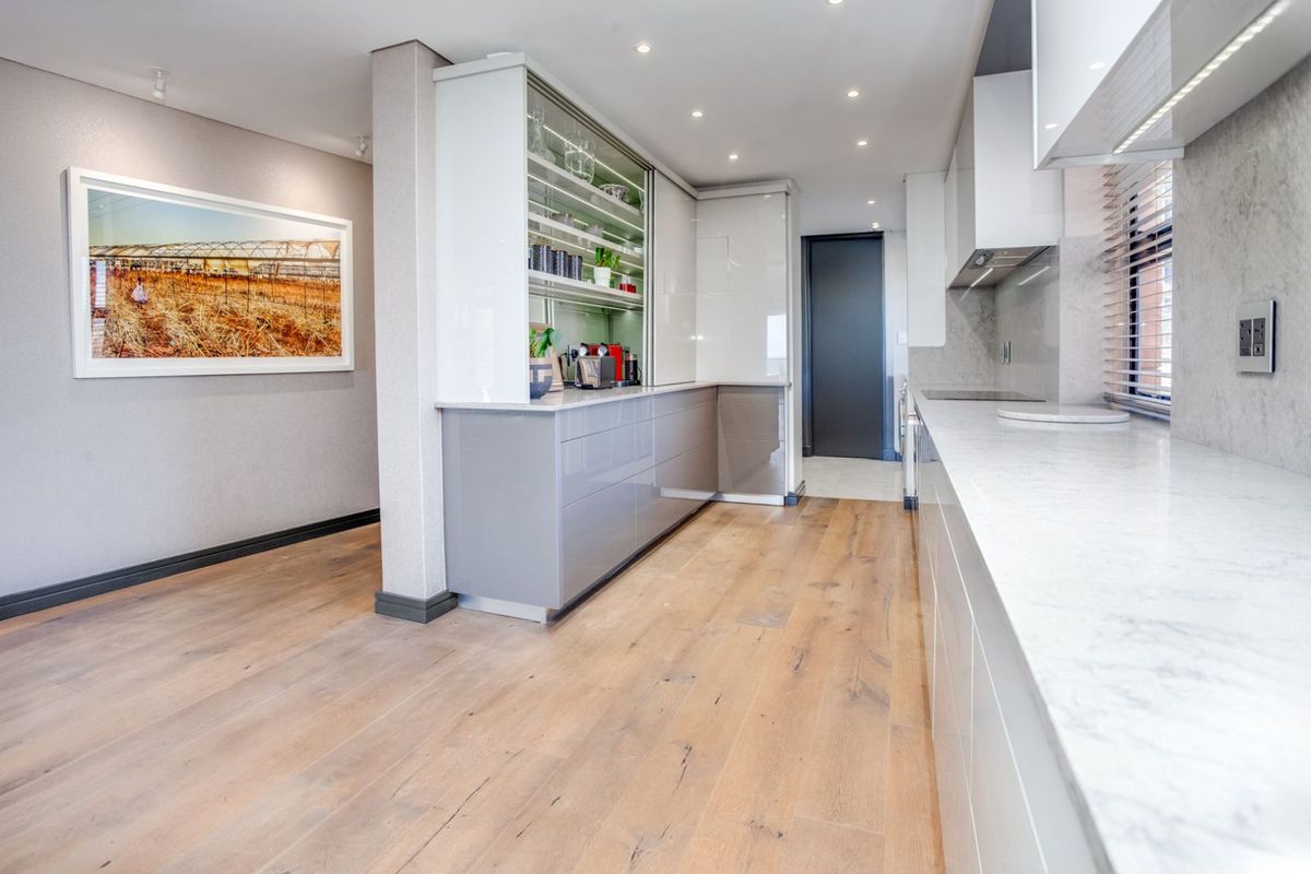Modern kitchen featuring sleek high-gloss cabinetry, stone countertops, integrated appliances, and light wood flooring in an open-plan layout.