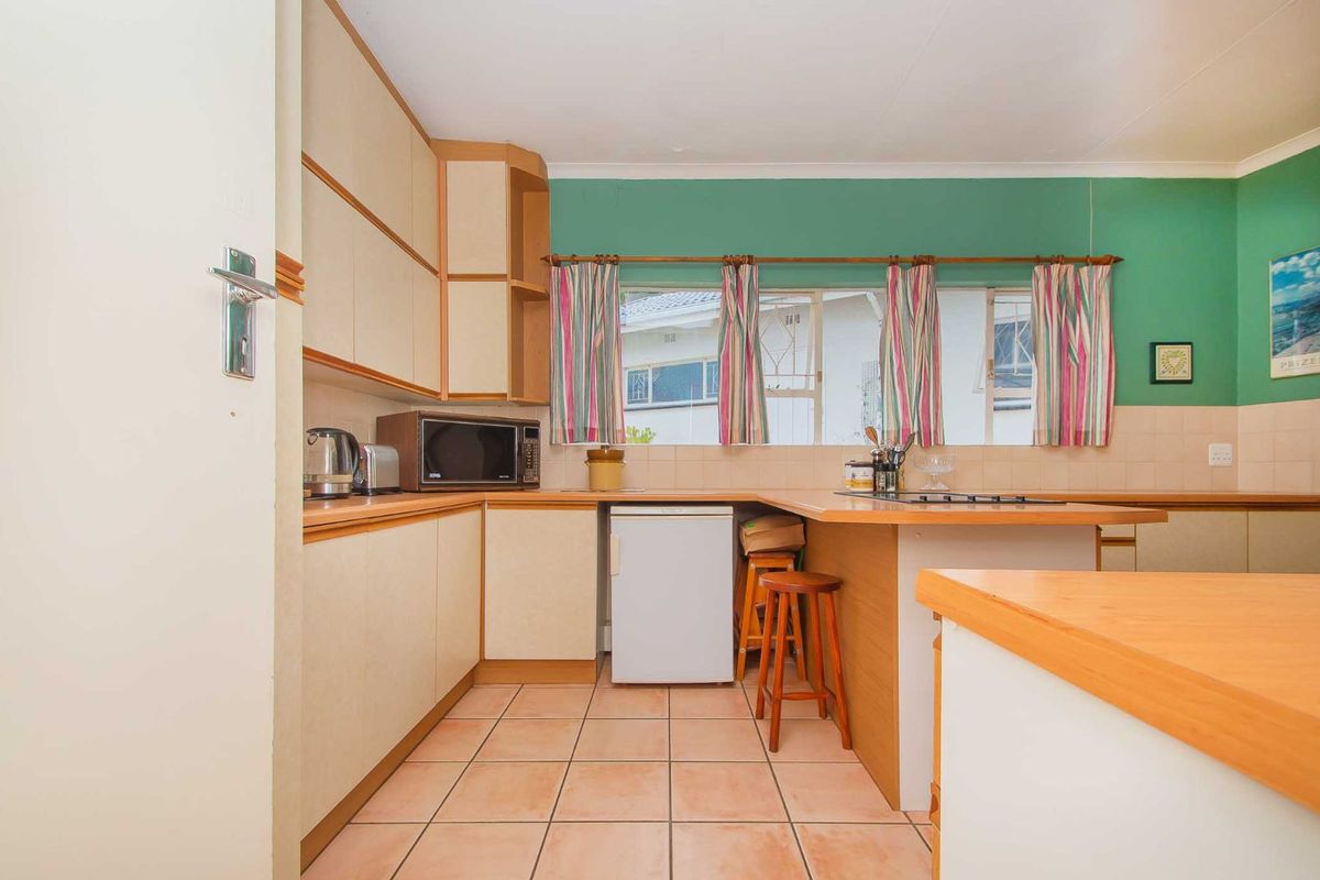 A functional kitchen featuring light-toned cabinetry, tiled flooring, and a built-in hob, offering a practical layout with ample counter space.
