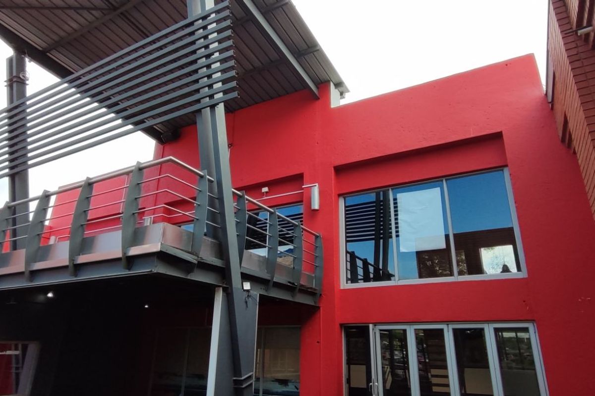 Exterior view of a modern commercial building featuring a prominent red facade, steel balcony structure, and large glass windows.