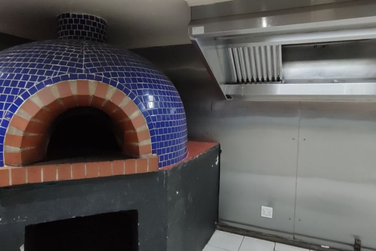 Commercial kitchen area featuring a built-in blue tiled pizza oven and a stainless steel extractor hood canopy.