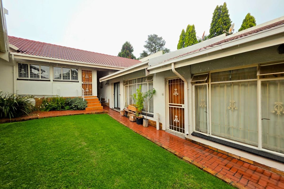 A view of the rear exterior of the house featuring a well-maintained lawn, brick pathways, and multiple access points with security gates.