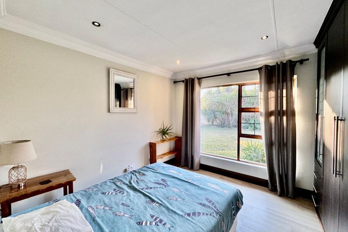 A well-lit bedroom featuring built-in cupboards, recessed ceiling lighting, and large windows overlooking the garden.