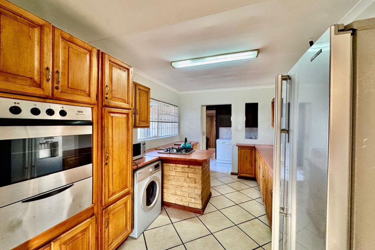 A functional kitchen featuring wooden cabinetry, a built-in oven, a gas hob on a brick-base island, and tiled flooring.