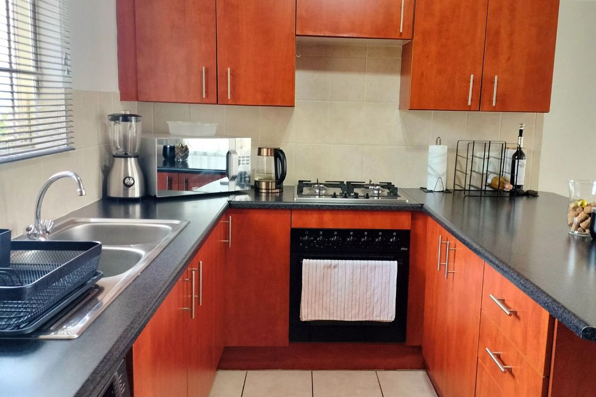 A functional kitchen featuring wooden cabinetry, dark laminate countertops, a built-in gas hob, and an integrated oven with a tiled backsplash.