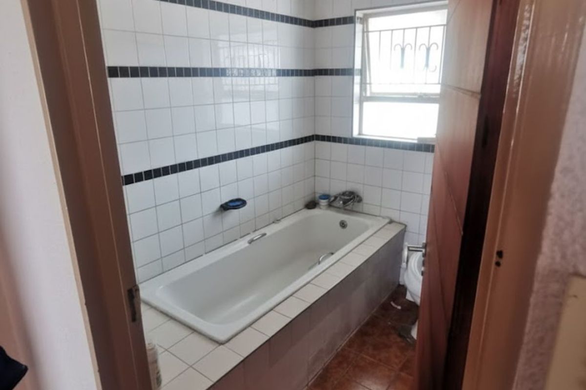 A dated bathroom featuring a built-in bathtub with tiled surround, ceramic wall tiles, and terracotta-style floor tiles, requiring renovation and cosmetic updates.