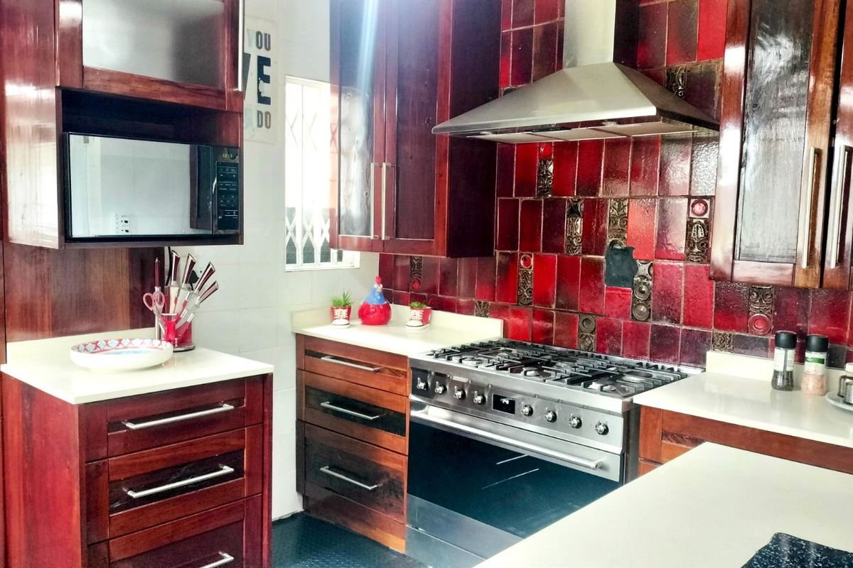 Kitchen featuring dark wood cabinetry, white countertops, a stainless steel gas range with extractor fan, and a distinctive red tiled backsplash.