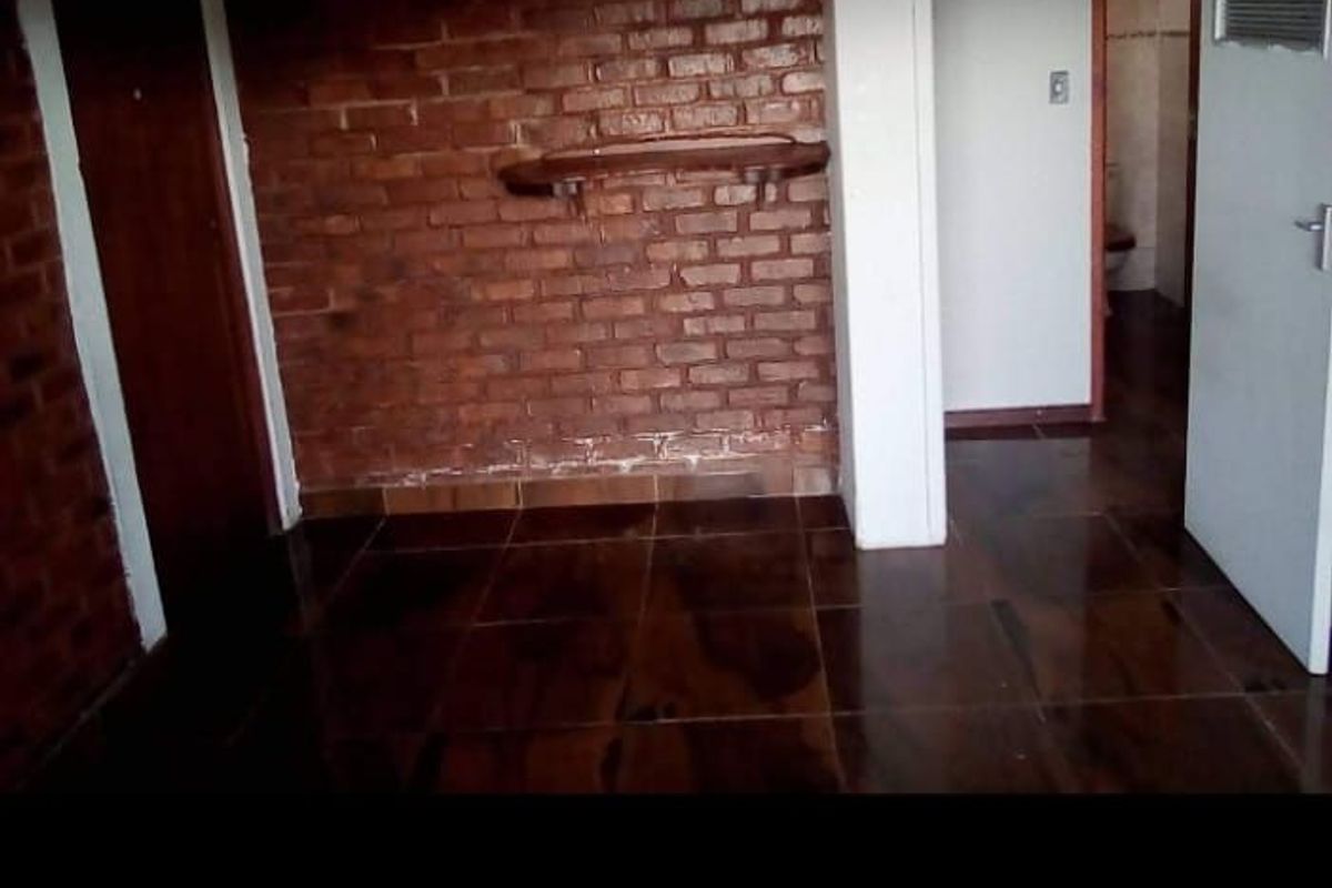 An interior room featuring exposed brick walls, dark tiled flooring, and access to an adjoining bathroom area.