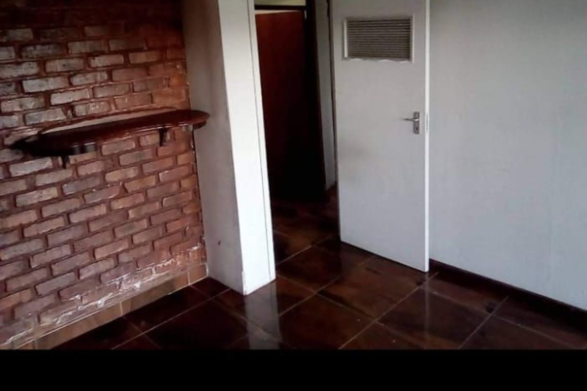 An interior room featuring a rustic exposed brick feature wall, dark tiled flooring, and a standard internal door leading to an adjacent space.