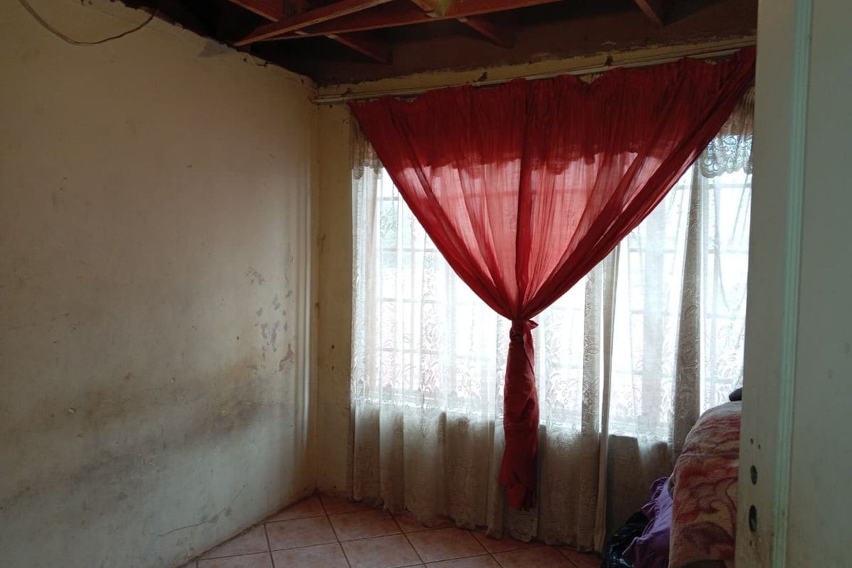 A bedroom space featuring tiled flooring and exposed ceiling rafters, requiring significant cosmetic renovation and finishing to reach its full potential.