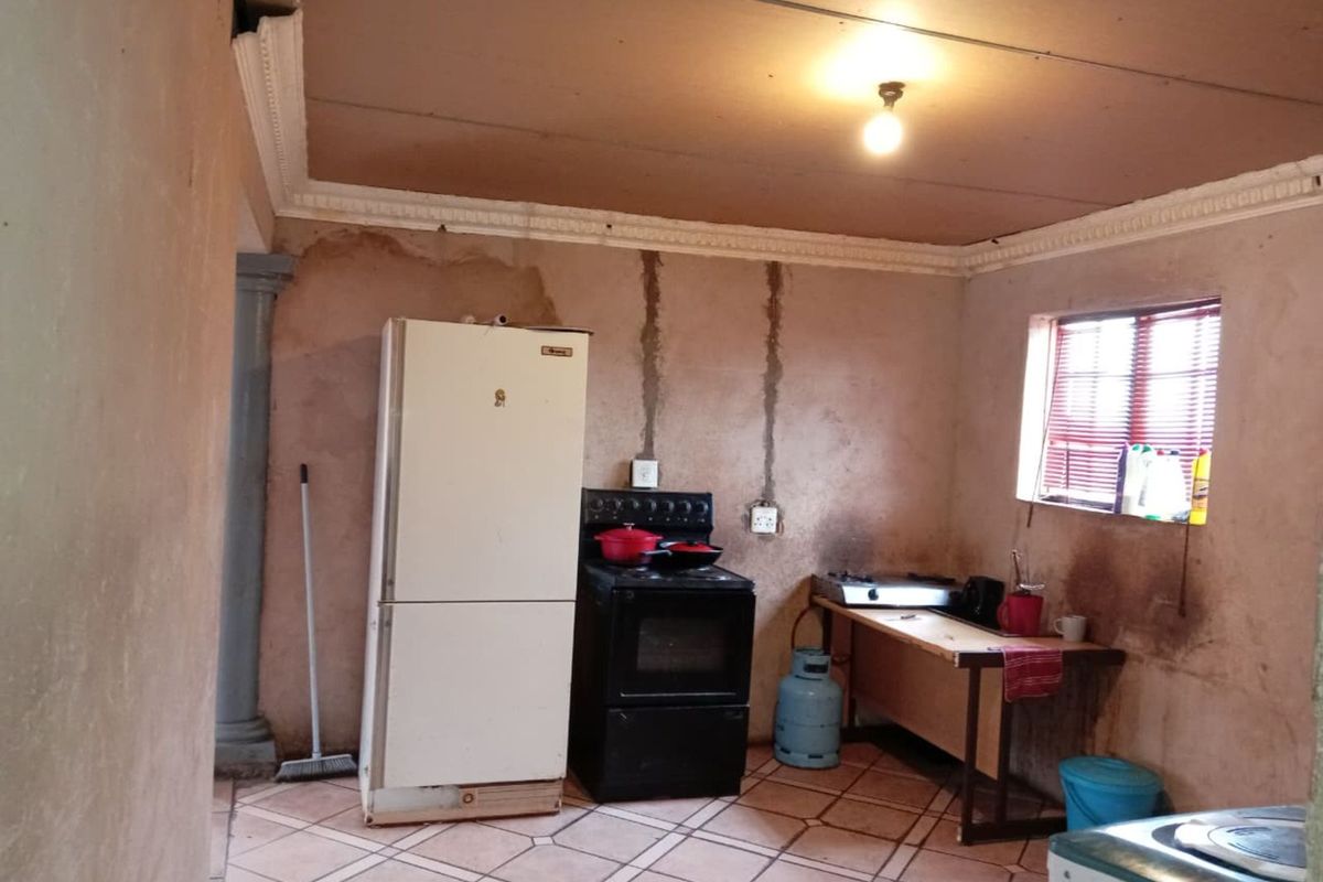 A basic kitchen area featuring tiled flooring, a freestanding stove, and visible wall damage requiring maintenance and cosmetic updates.