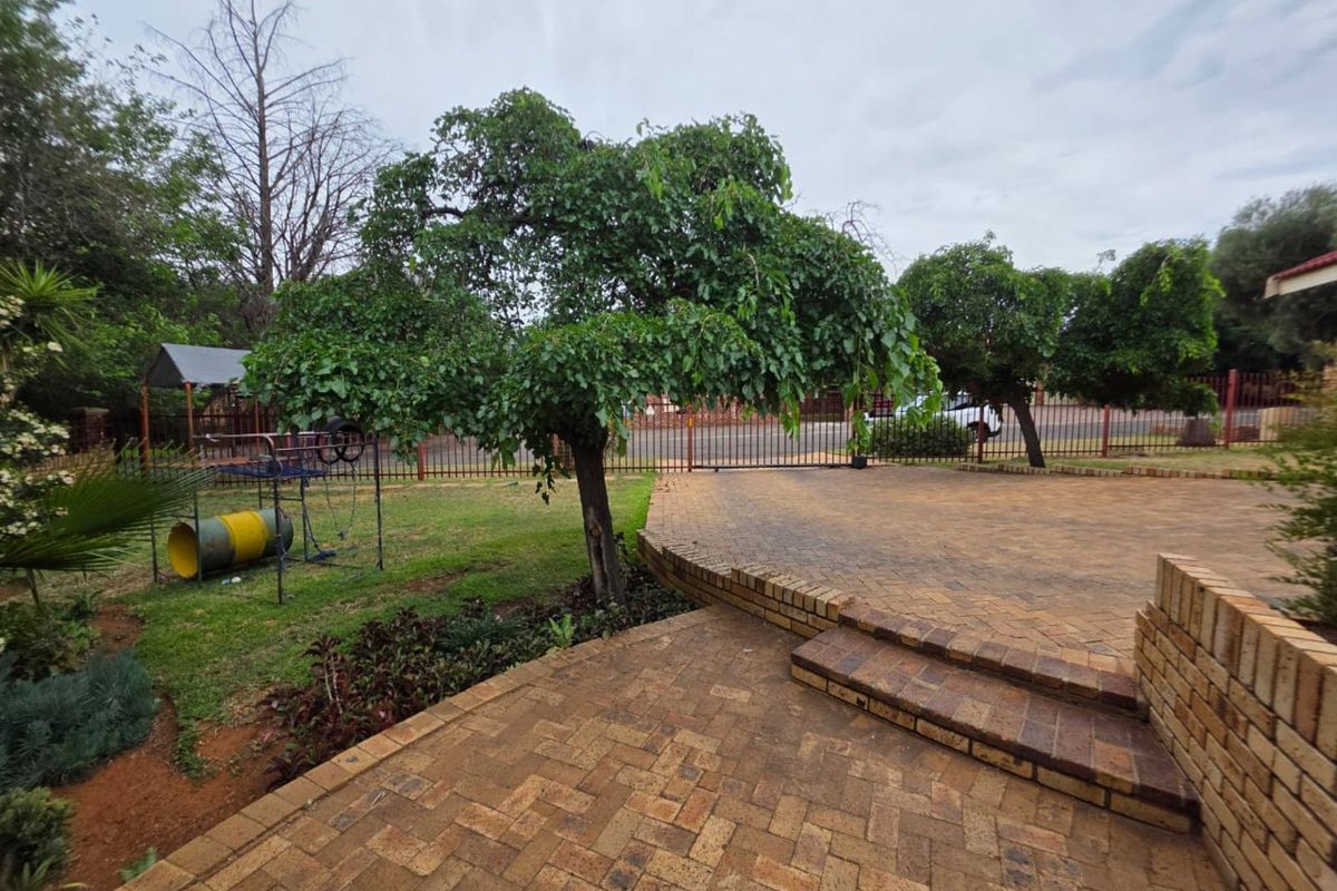 A spacious rear garden featuring a multi-level paved patio area, established trees, and a lawn, enclosed by perimeter fencing.