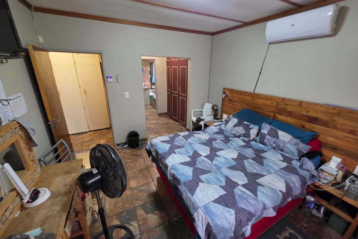 A bedroom featuring tiled flooring, a wooden headboard, and a wall-mounted air conditioning unit, with direct access to an adjoining room.