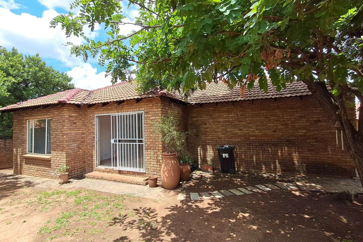 Rear view of a face-brick townhouse featuring a tiled roof, sliding glass door with security gate, and a mature garden area.