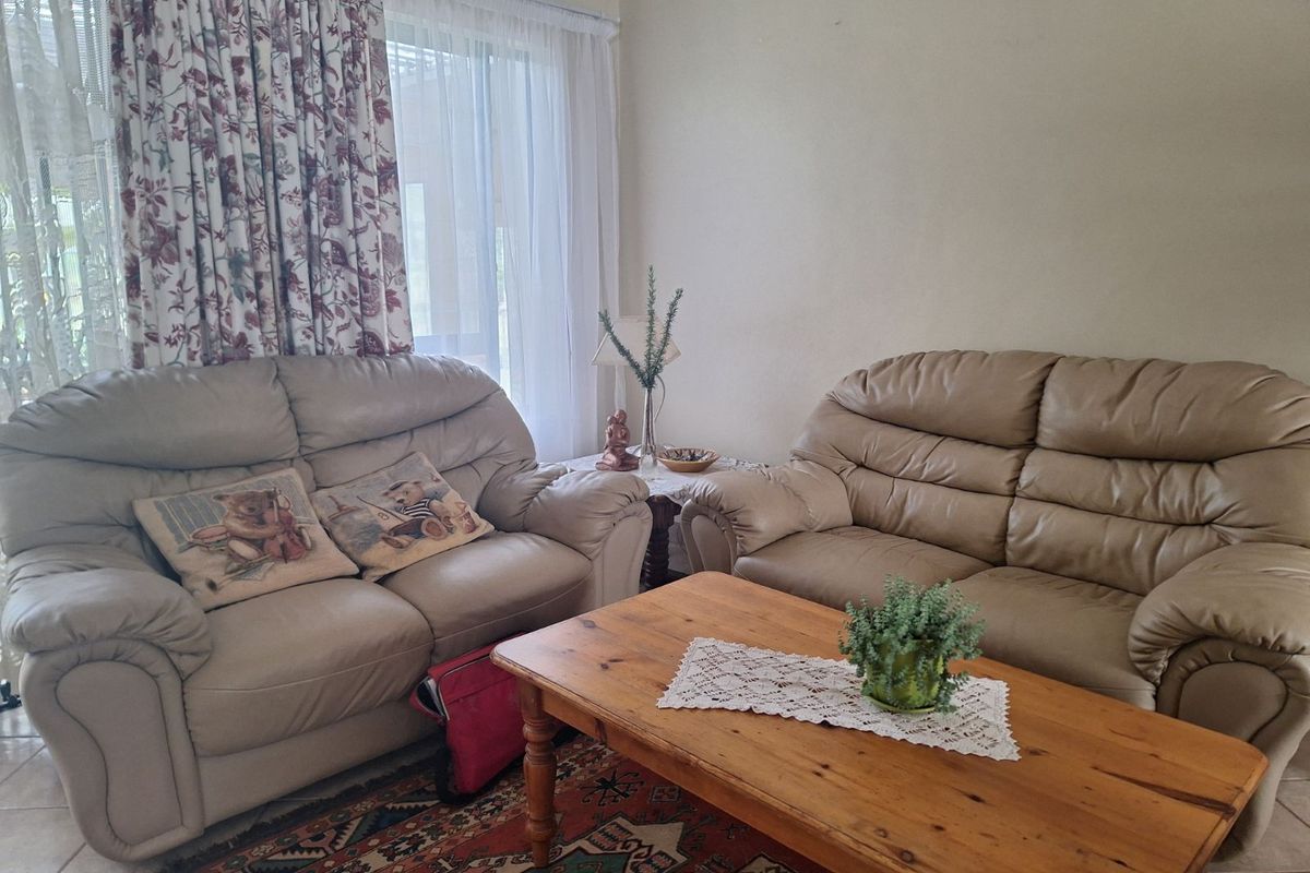 A comfortable living room featuring tiled flooring and large windows with curtains, providing natural light to the space.