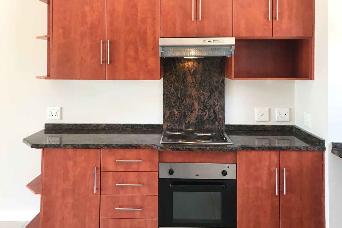 A functional kitchen featuring cherry-wood cabinetry, granite countertops, a built-in oven, electric hob, and a stainless steel extractor fan.