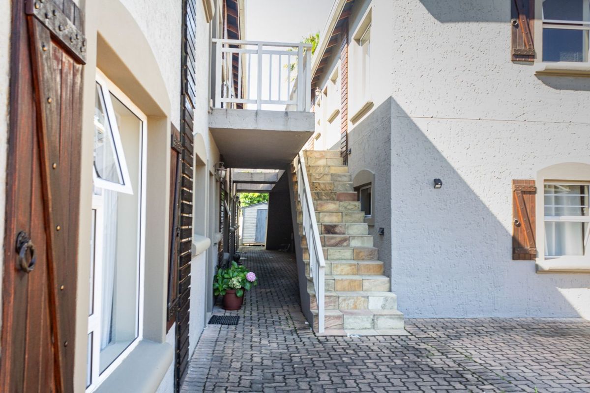 Exterior view of an apartment complex featuring a paved walkway, stone-clad staircase, and a balcony with white railings.