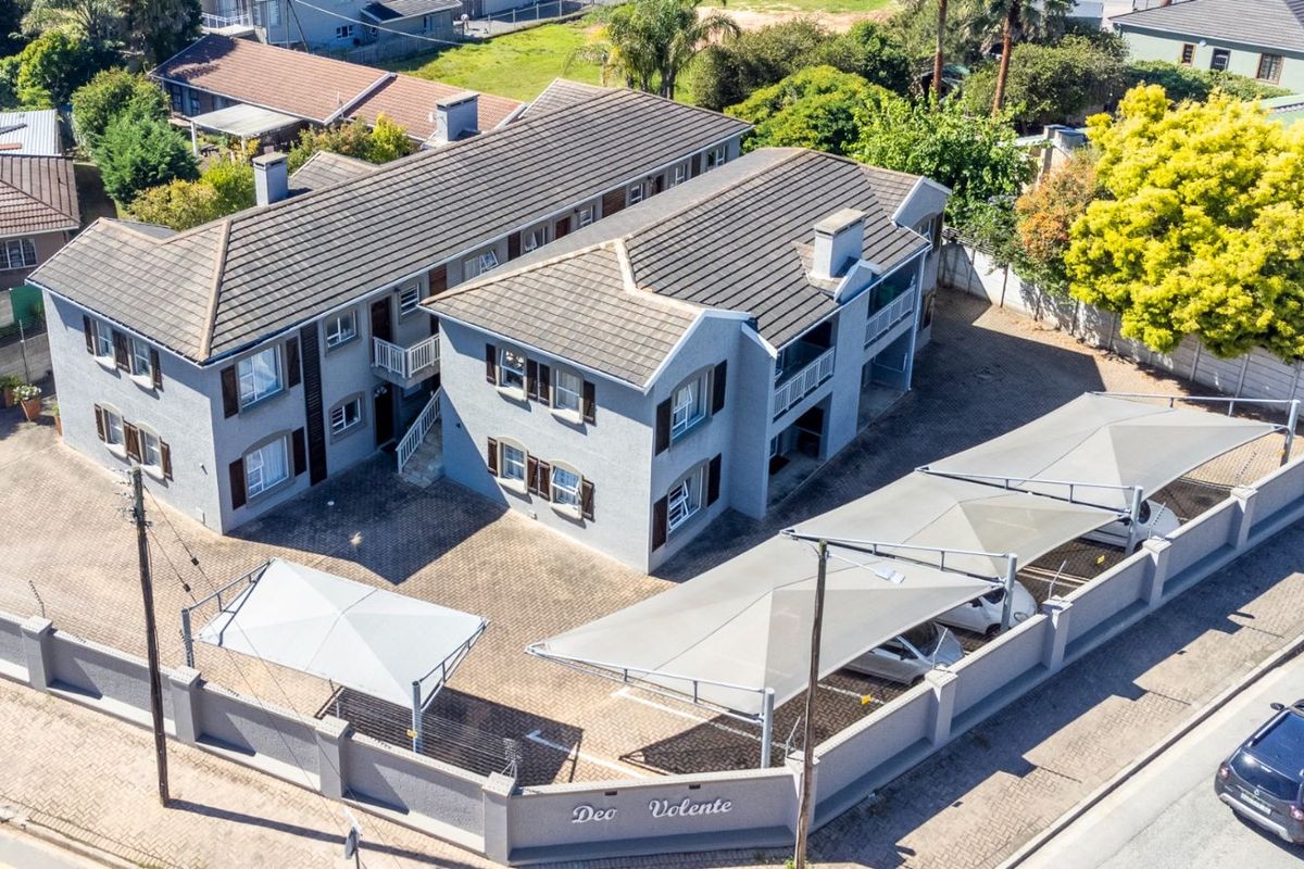 Aerial view of a multi-story apartment complex featuring a paved courtyard, covered parking bays, and perimeter walling.